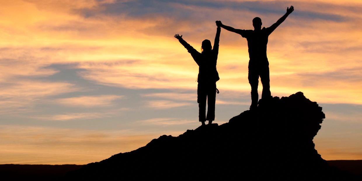 Two people celebrating on a summit at sunset.