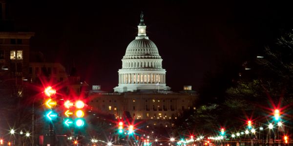 The illuminated US Capitol building at night with colorful traffic lights in the foreground.