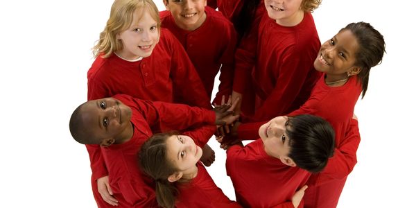 Group of children in red shirts forming a circle and smiling.