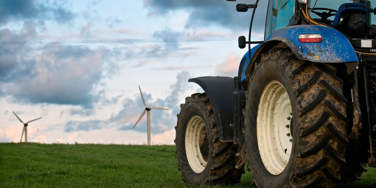 Blue tractor on a green field with wind turbines in the background.