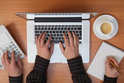 Person multitasking with laptop, phone, and notes, accompanied by a cup of coffee.