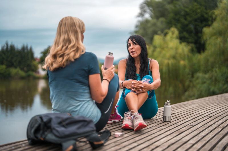 Mature women talking and bonding after an active day of exercise. They are drinking water and relaxing in nature.