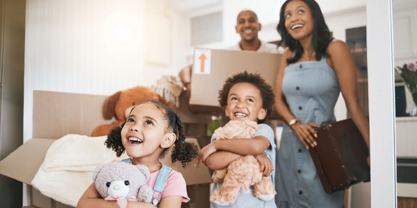 Happy family with two young children holding stuffed animals, smiling as they move into new home