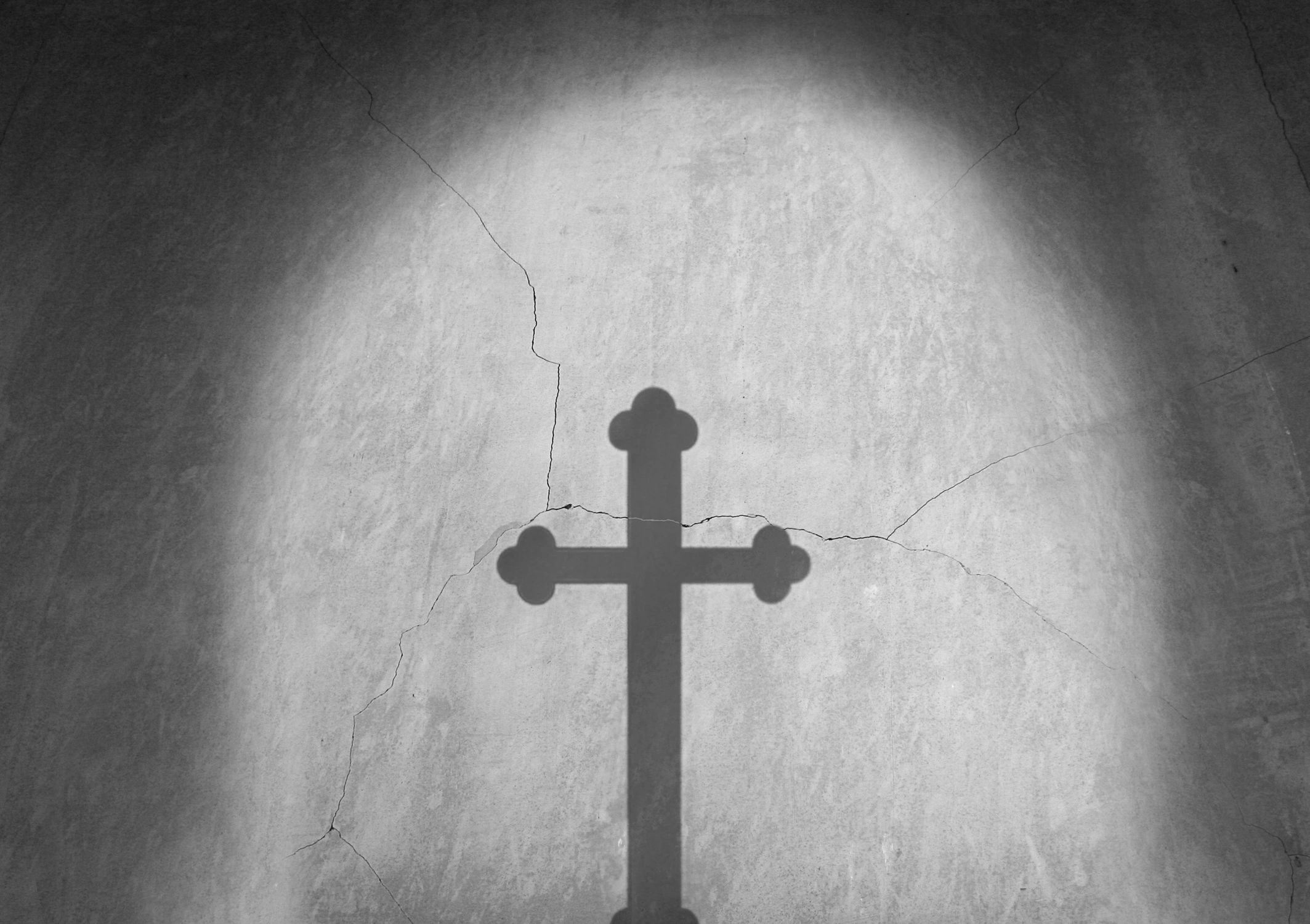 Shadow of a cross on a cracked, textured wall illuminated by light.