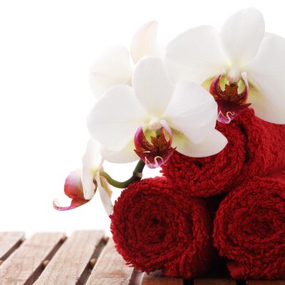 White orchids resting on rolled red towels on a wooden surface.
