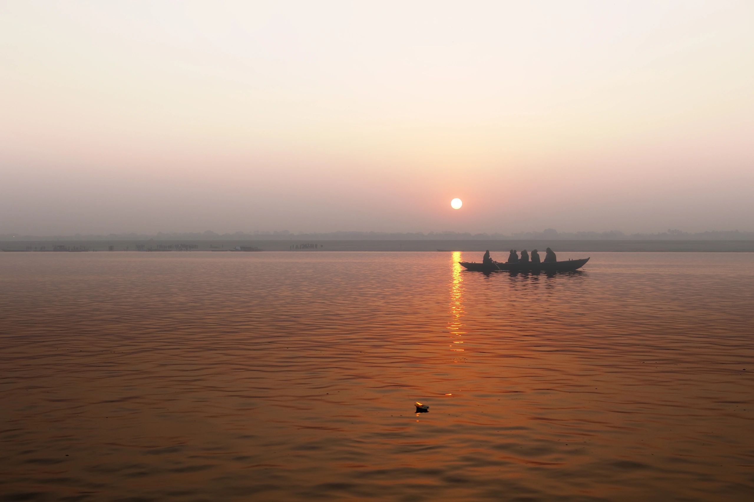 Silhouetted people in a boat on a calm river at sunset.