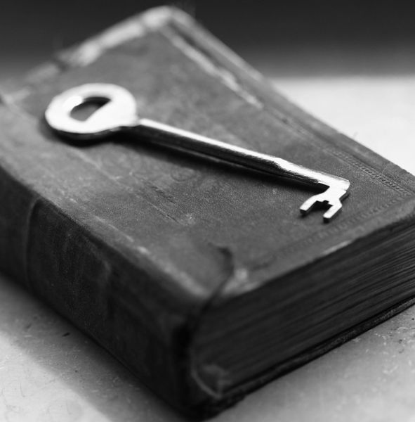An old key resting on a worn-out book in black and white.