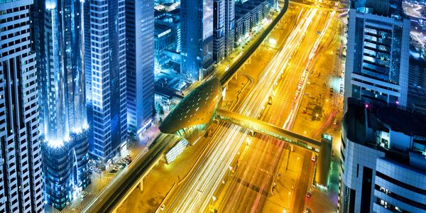 A vibrant cityscape at night with illuminated skyscrapers and busy light trails on the highway.
