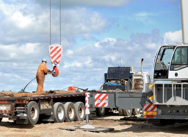 Worker operating a crane hook on construction site.