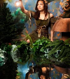 A woman in a fantasy costume holding a lantern in a mystical forest setting.