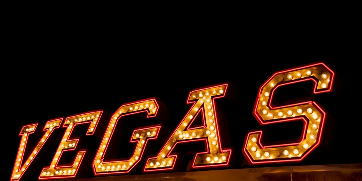 Illuminated Vegas sign with bright bulbs against a dark background.