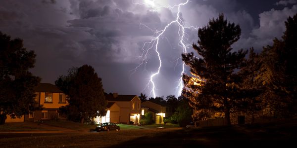 Lightning striking behind houses at night.