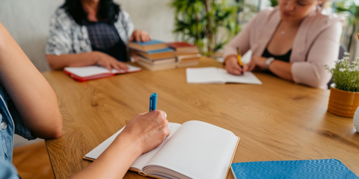 People writing notes during a meeting at a wooden table.