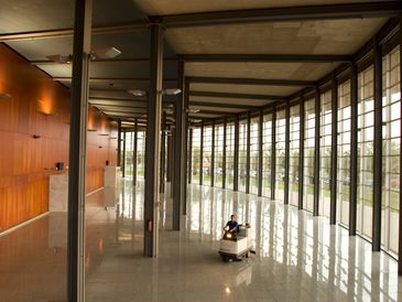 A person operating a floor cleaning machine in a spacious, modern building with large windows.