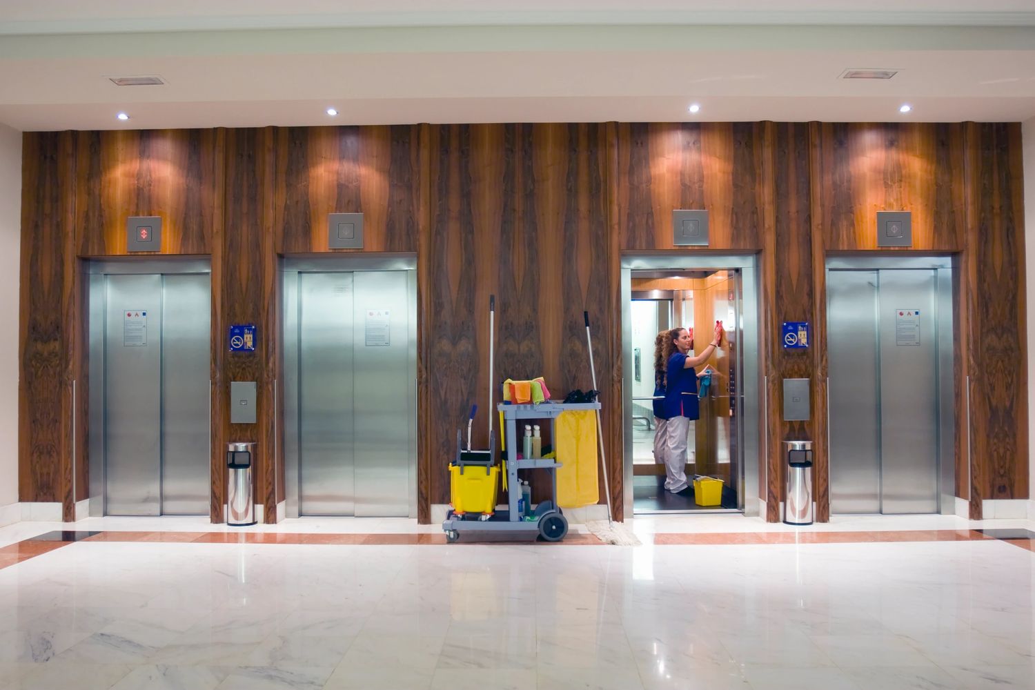 A janitor cleaning the inside of an elevator in a modern building lobby.
