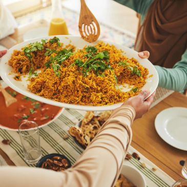 People sharing a large plate of biryani at a dining table.