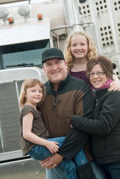 Smiling family of four posing in front of a large truck outdoors.