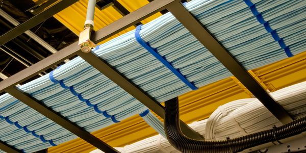 Organized blue and white cables neatly secured on a ceiling rack in a data center.