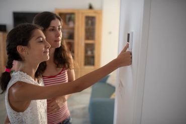 Two girls adjusting a thermostat on the wall.