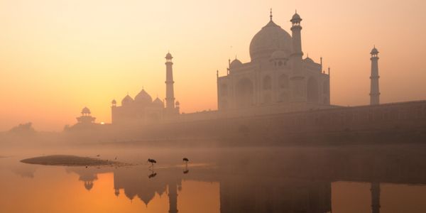 A misty sunrise view of the Taj Mahal reflecting in the water.
