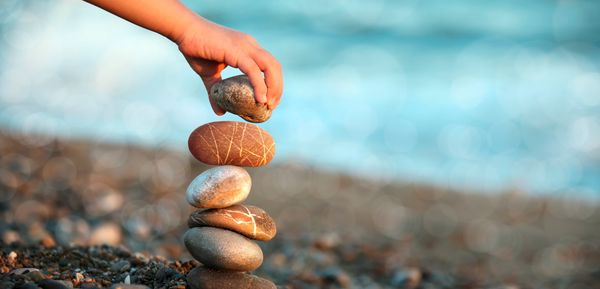 Hand stacking smooth stones by the sea.