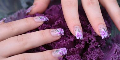 Hands with floral nail art on purple curly leaves.