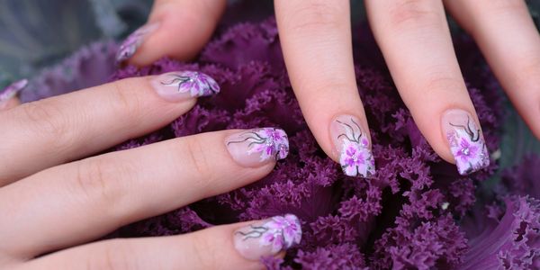 Hands with floral nail art on purple curly leaves.