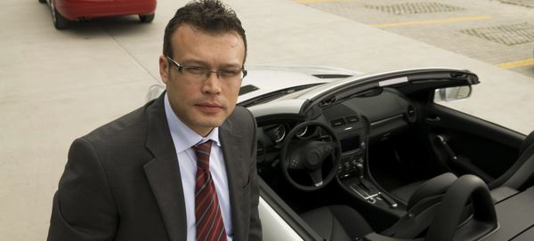 Confident businessman standing next to a convertible car in a parking area.