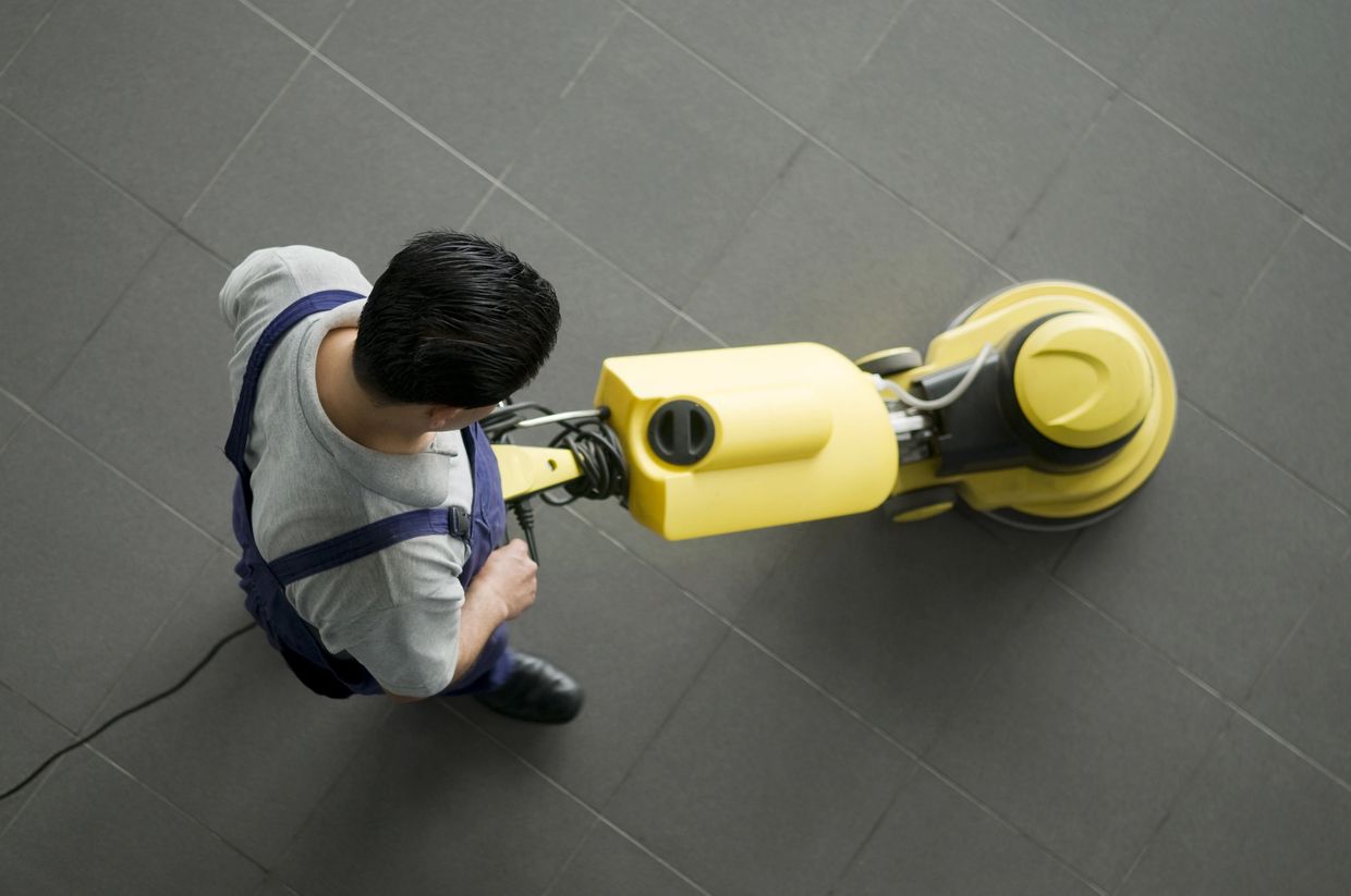 Man using a yellow floor polishing machine on tiled floor.