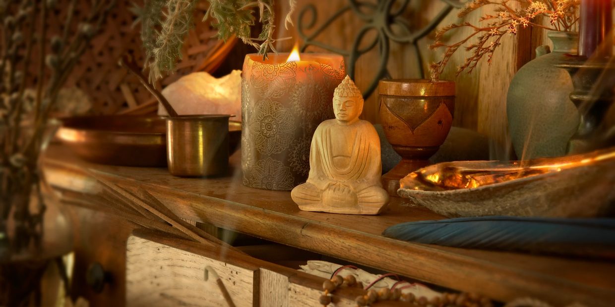 Cozy meditation altar with Buddha statue, lit candles, and natural decor on wooden furniture.