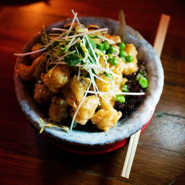 A bowl of crispy fried cauliflower topped with sprouts and green peas.