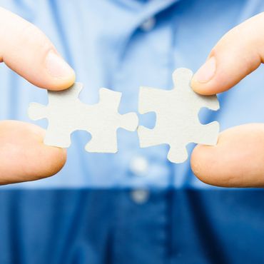 Close-up of hands connecting two white puzzle pieces.