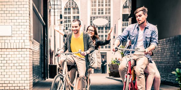Three friends joyfully riding bikes through an alley.