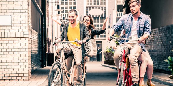 Two couples riding bicycles together happily in a city alleyway.