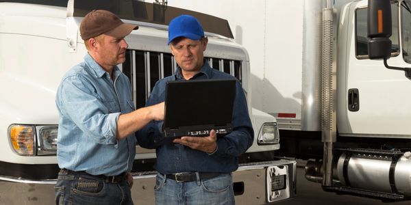 Two truck drivers using a laptop by trucks.