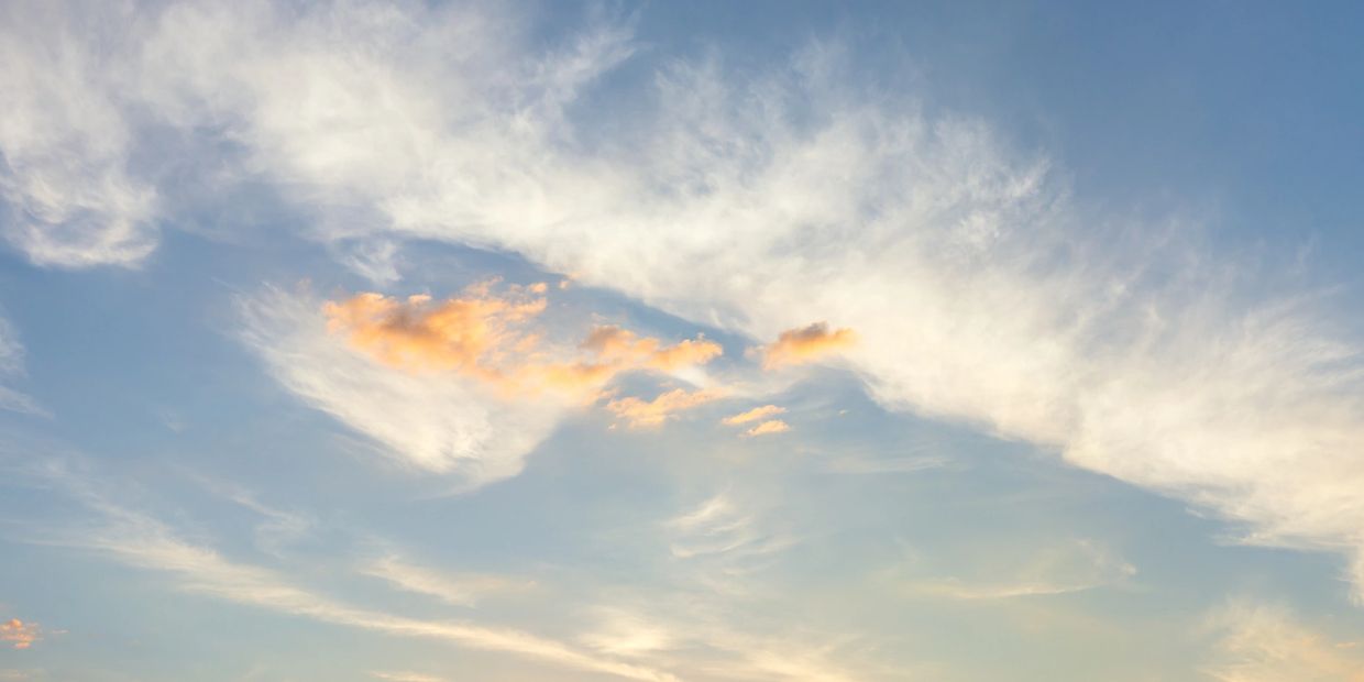 Soft clouds with hints of orange glow during sunset in a clear blue sky.