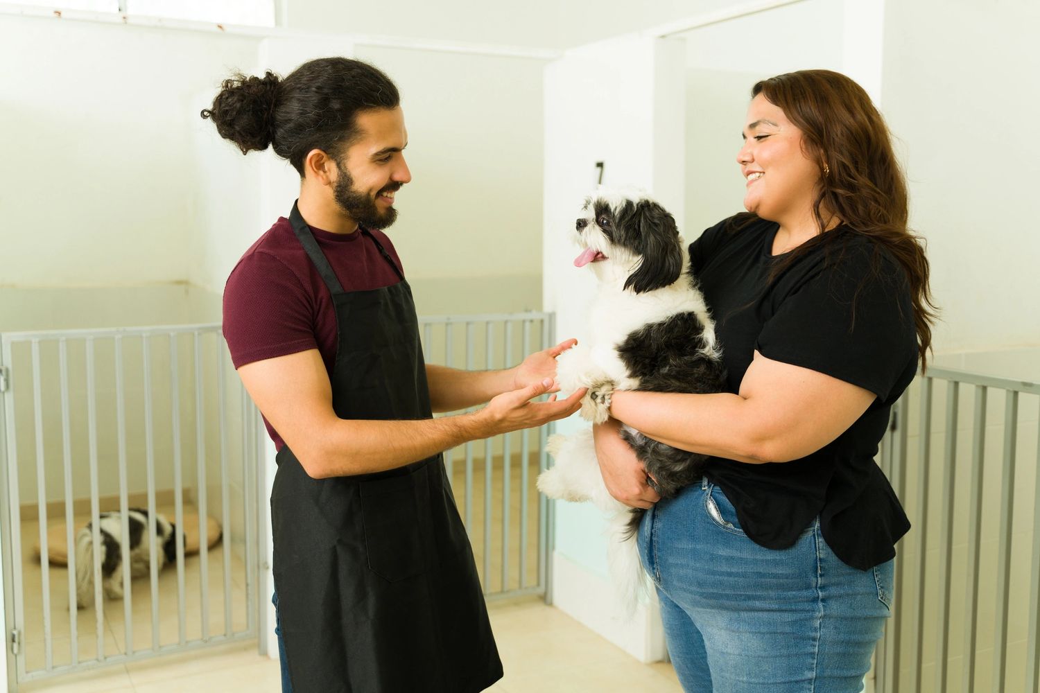 A woman holding a dog while talking to a man in an apron at a pet care facility.