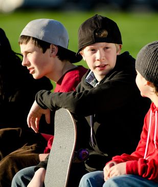 Two boys with scooters overlooking a busy skate park with many people skating.