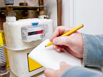 Person recording gas meter reading with a yellow pen on a notepad.