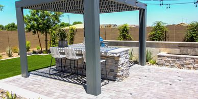 Modern backyard patio with pergola, stone bar, and white chairs.
