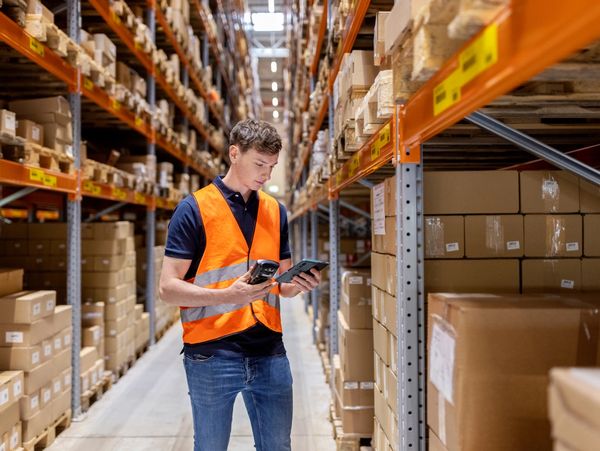 Warehouse worker in orange vest scanning packages with a handheld device.