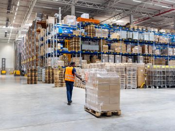 Worker moving pallets in a large warehouse.