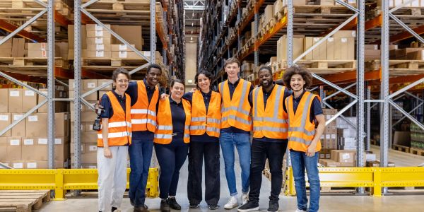Diverse warehouse team in orange safety vests posing together.