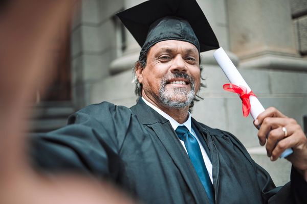 Smiling graduate holding diploma outside building.