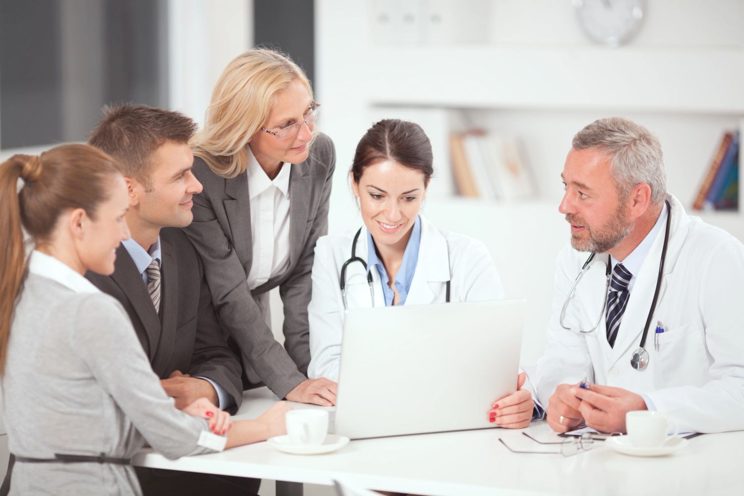 Team of doctors and business professionals collaborating over a laptop.