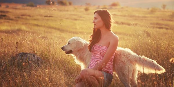 Woman sitting in a field with her golden retriever during golden hour.