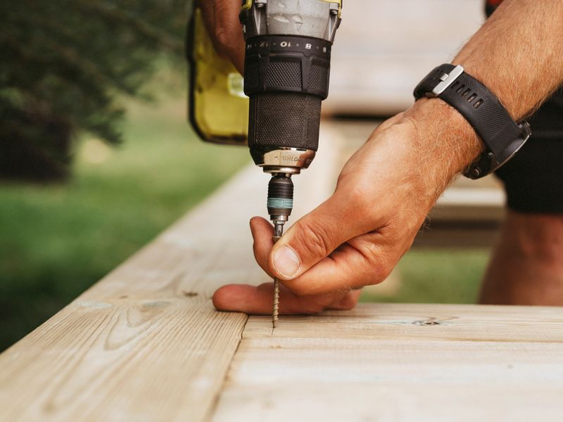 Screwdriver and man building a wooden patio deck outdoors in his garden
Working and buidling under contstruction. Home improvement.