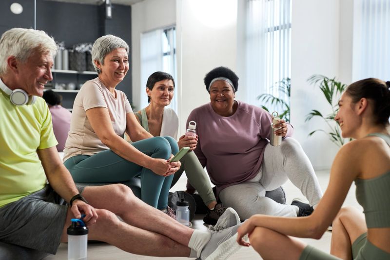 Group of elderly people resting after training and talking to coach in studio