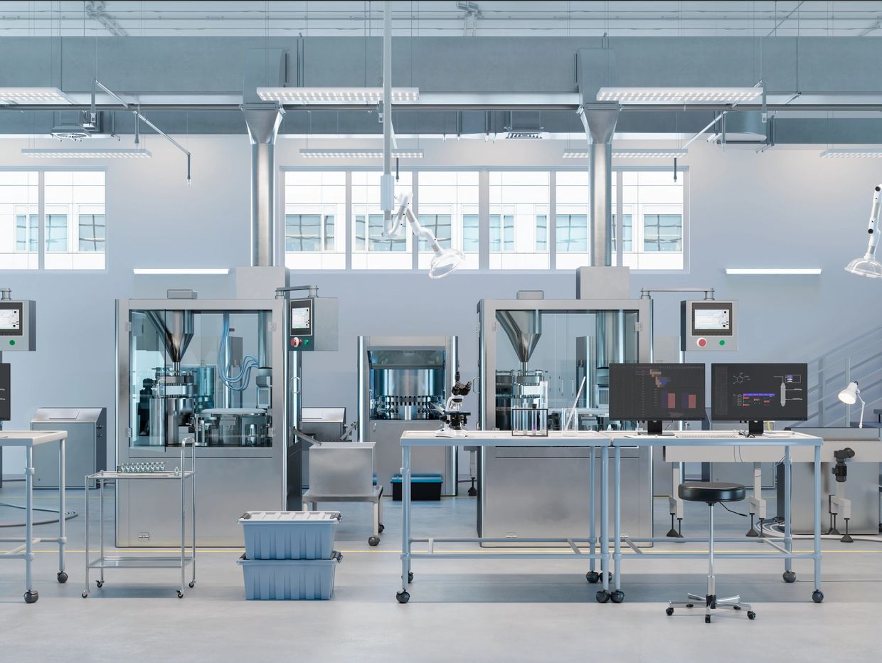 Modern pharmaceutical manufacturing lab with advanced machinery and computer workstations.