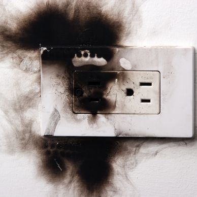 Burnt electrical outlet with black soot marks on white wall.
